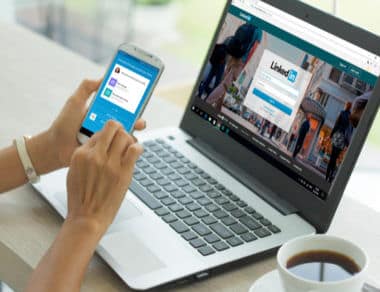 woman using her smartphone and in front of her laptop